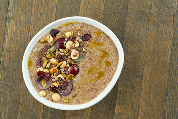 Appetizing flaxseed porridge with olive oil, seeds, grapes and hazelnuts in a white bowl on a wooden background. Vegetarian food. Eastern cuisine