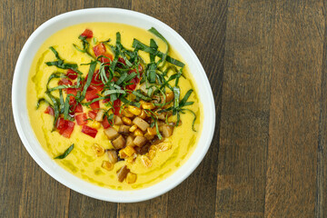 Appetizing and dietary dish - corn soup with cream and fried mushrooms, tomatoes and herbs in a white bowl on a wooden background
