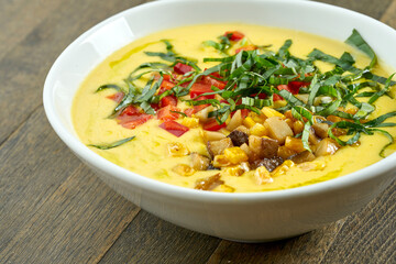 Appetizing and dietary dish - corn soup with cream and fried mushrooms, tomatoes and herbs in a white bowl on a wooden background