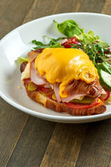 Delicious and great breakfast - croissant sandwich with ham, melted cheese, tomatoes with mixed salad, served in a white bowl on a wooden background