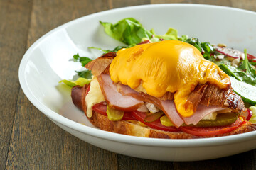 Delicious and great breakfast - croissant sandwich with ham, melted cheese, tomatoes with mixed salad, served in a white bowl on a wooden background
