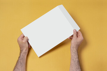 Closeup shot of a male hand holding an A4 paper envelope on the yellow background