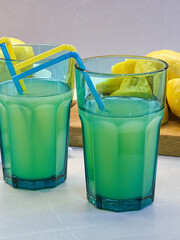 Primer plano de dos vaso con zumo de limón verde y cañitas de colores azul y amarillo sobre una encimera gris claro