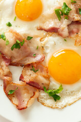 Fried eggs with bacon on a white plate close up