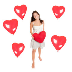 Full length portrait of a young laughing woman holding a red heart, she is surrounded by heart balloons, isolated on white studio background