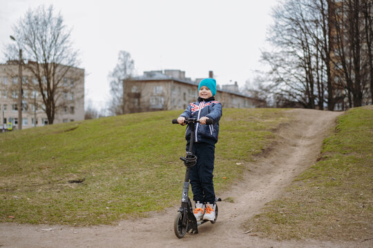 Cute 8 years old little Caucasian boy riding down the hill  in park on black kick scooter Image with selective focus.