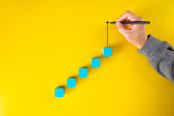 Man hand drawing an upward pointing arrow on top of growing graph made of wooden block.