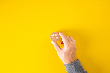 Fototapeta na wymiar Male hand holds a wooden block with the word apply now on yellow background.