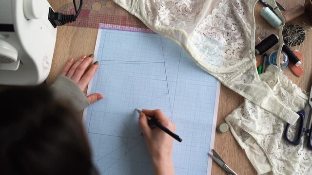 Top view of female hands are drawing design of a new collection of lingerie. Workplace of a professional designer. Copy space.