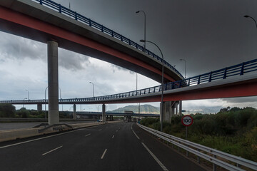 Several bridges crossing a highway with a cloudy sky.