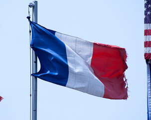 Bandiera francese blu bianca e rossa, sgualcita e sbiadita che sventola al vento agganciata a un palo di ferro