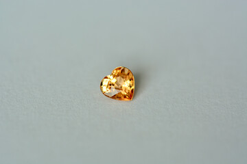 Genuine natural sapphire golden orangery yellow color bright transparent heart shaped faceted gemstone setting for jewelry making. Small one carat stone on daylight. Gray background.