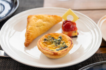 Spinach quiche, Pie and Cheesecake mini snack set on white plate in a garden.