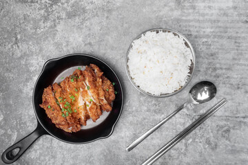 Top view homemade breaded fried chicken chop topped spring onion on the mini black pan  and a bowl of steamed rice