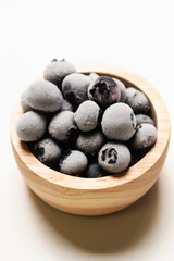 Frozen blueberries in wooden bowl isolated on white background.