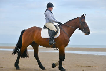 Young woman lives her dream riding her beautiful bay horse on an empty beach in rural Wales.