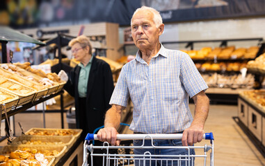 older man shopping buns and bread in bakery section of supermarket