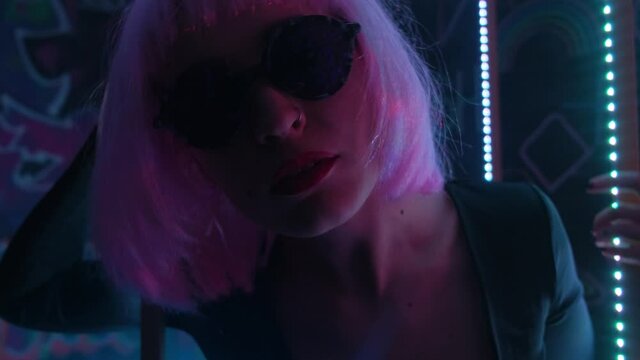 Hipster girl with glasses and a pink wig in a dark neon room with smoke.
