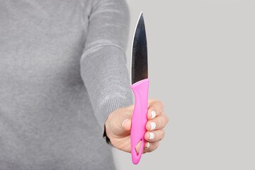 Hand with small kitchen knife on grey background