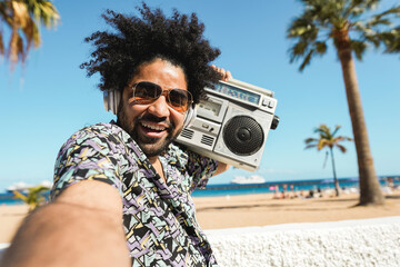 African american man listening music with vintage boombox stereo outdoor with beach in background -...