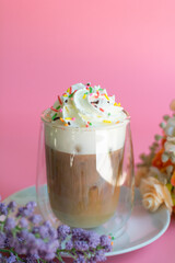 Ice coffee with a layer of milk and whipping cream with color sugar topping on pink background. Beverage and drink at the party concept.