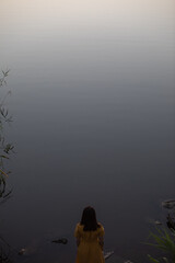 young woman in yellow dress taking picture of grey lake. evening dusk time