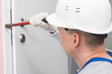 a construction worker in a helmet opens the front door with a special tool