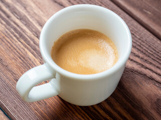 a white cup with a delicious and aromatic espresso on a wooden background. side view