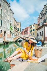 Fototapeta na wymiar woman sitting on pond with view of venice canal eating pizza