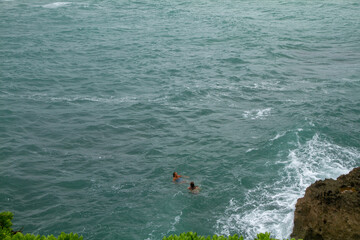 girls swimming in the ocean with waves crashing on rocks
