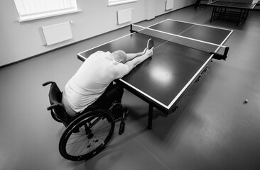 Adult disabled man in a wheelchair training before play at table tennis