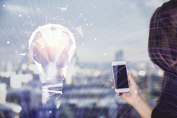 Double exposure of light bulb hologram and woman holding and using a mobile device. Idea concept.