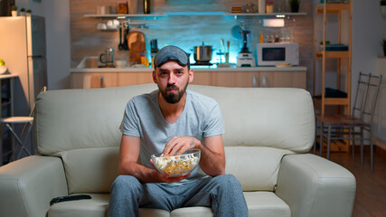 Portrait of man with beard holding popcorn bowl while watching entertainment movie on television....