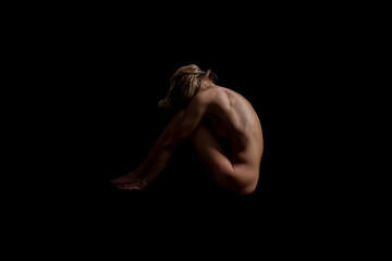A completely naked woman sits with her head bowed. Black background