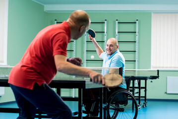 Adult disabled man in a wheelchair play at table tennis with his coach