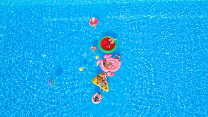 AERIAL: Cheerful young friends having a watergun fight on fun floaties in pool