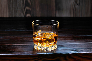 Glass of whiskey with ice cubes on a dark wooden table