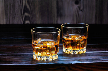 Two glasses of whiskey with ice cubes on a dark wooden table