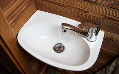 Fototapeta premium Small white wash basin, wooden walls around, closeup detail