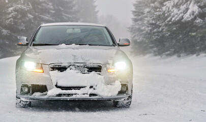 Silver car parked on snow covered winter road, blurred trees background, front view, headlights shining - Powered by Adobe
