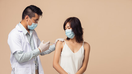 Asian people, Man doctor protection coronavirus (COVID-19) vaccine injection to female on brown background. Asian woman getting vaccinated by medical professional.