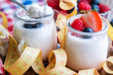 yogurt with raspberries and blueberries on wooden background with measuring tape, diet and food concept