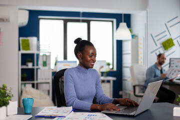 African woman working typing on laptop computer, concentrated to finish important deadline. Diverse team of business people analyzing company financial reports from computer.
