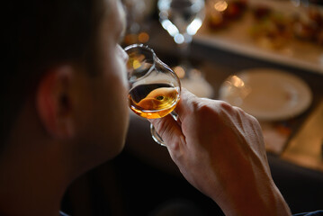 Man holding glass of cognac close to nose smelling the aroma - Powered by Adobe