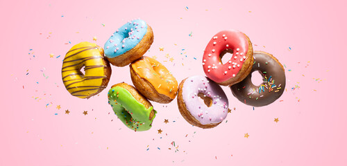 Colorful decorated donuts falling in motion on pink background with sprinkling. Sweet and various doughnuts flying on pastel backdrop. Panorama banner - obrazy, fototapety, plakaty