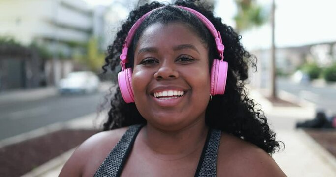 Curvy african girl smiling in camera while doing jogging routine outdoor in the city - Plus size and sport workout concept