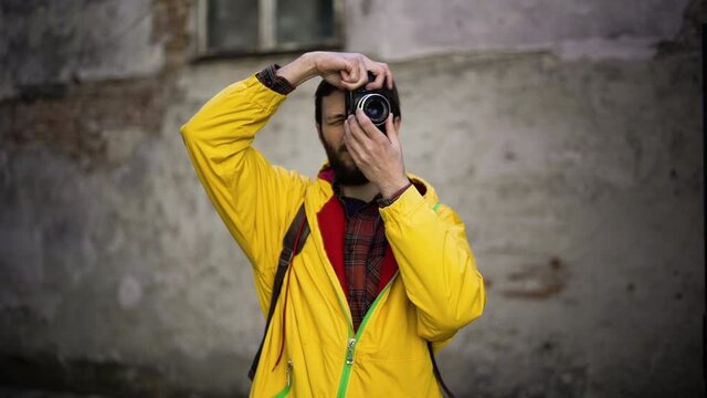 Adult male tourist photographer in yellow jacket taking photos with old film camera. Male backpacker with film camera traveling at the ancient city