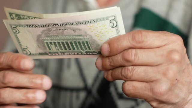 Close-up of an elderly man's hand holding a 1 and 5 American dollar bill. A pensioner plans a budget by counting money. 5 dollars in the hands of a pensioner. Selective focus, shallow depth of field