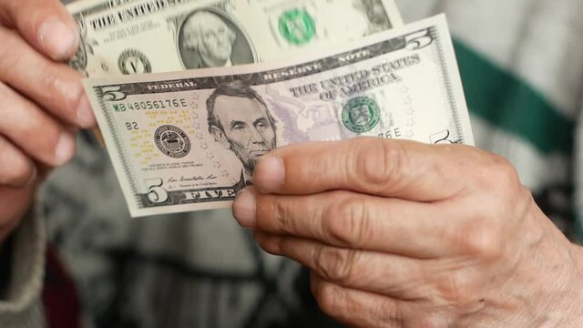 Close-up of a man holding paper bills of 1 and 5 dollars. American money in the hands of a man. The pensioner counts small money. Selective focus