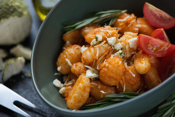 Closeup of potato gnocchi served with sun dried tomato pesto and belper knolle in a green bowl, selective focus